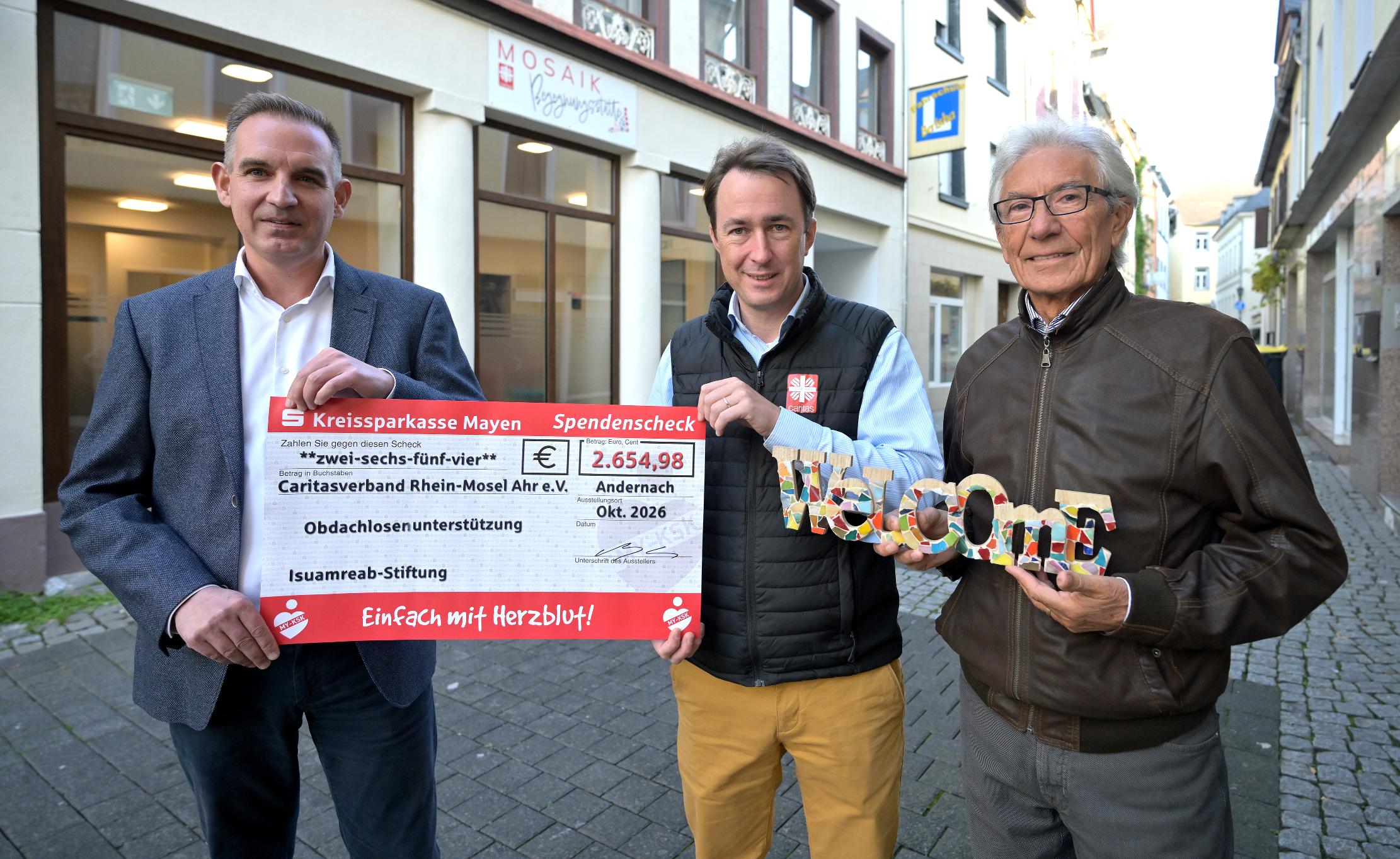 René Goldberg, Leiter des VermögensberatungsCenters der Kreissparkasse Mayen (l.), und Enzo di Prato, Vertreter der Isuamreab-Stiftung (r.), überreichten im Namen der Stifterin den symbolischen Scheck sowie ein Wilkommensschild für die neue Begegungsstätte „Mosaik“ an Caritasdirektor Christian von Wichelhaus (Mitte). Link zum Artikel